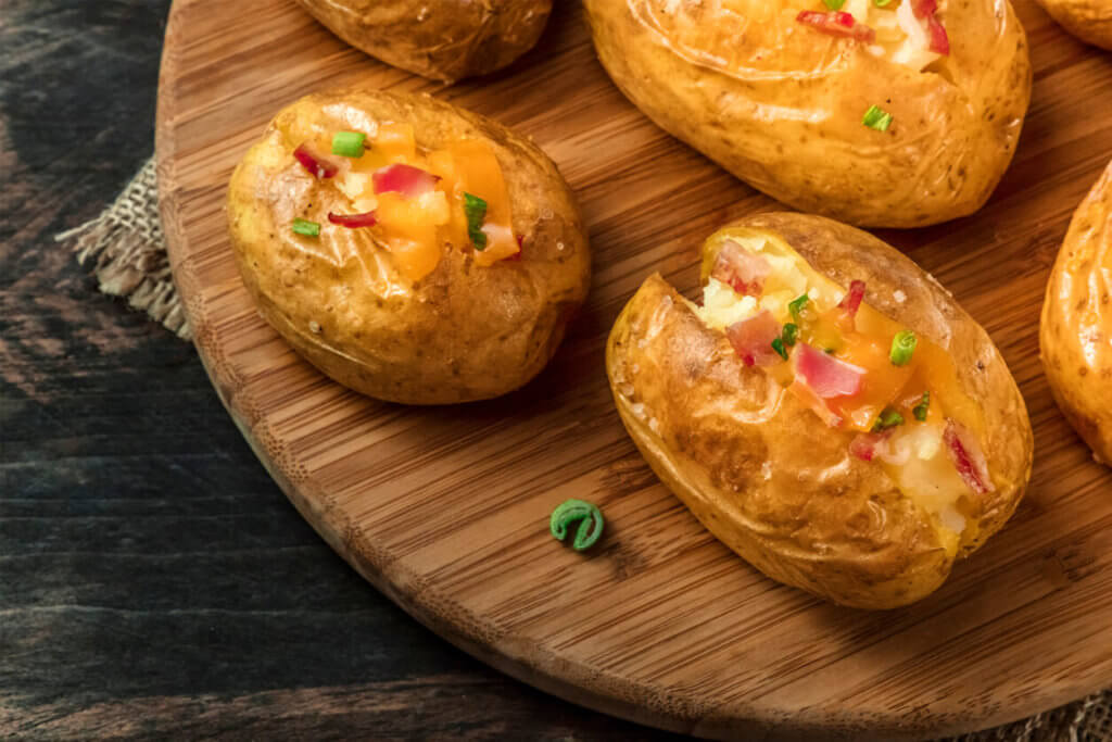 Baked potatoes with ham and green onion, close-up shot on a dark rustic wooden background with a place for text