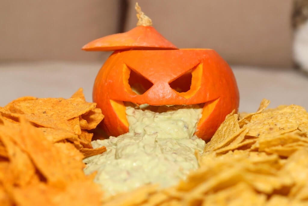 Carved pumpokin filled with guacamole and tortilla chips. Halloween party food. Selective focus.
