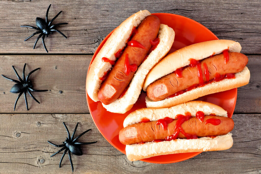 Creepy Halloween hot dog fingers on an orange plate over a rustic old wood background
