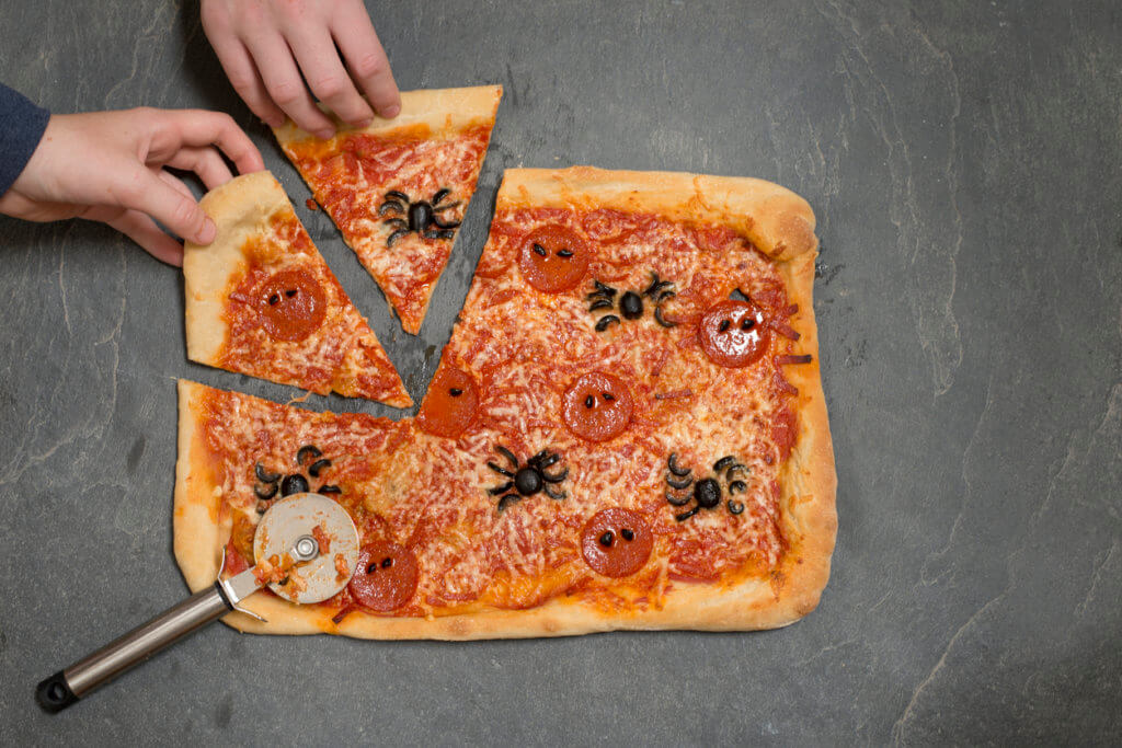 Hands taking slices of halloween-themed pizza with pizza cutter