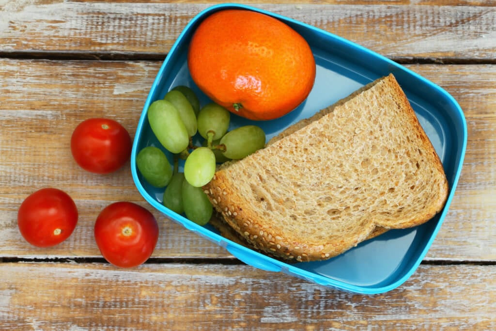 Healthy school lunch box containing brown sandwich, cherry tomatoes, fruit