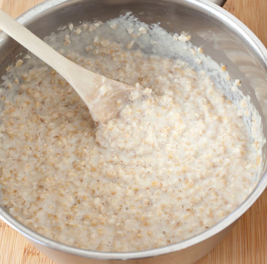 "Steel-cut oatmeal in still in the pot from cooking with a wooden spoon.Steel-cut oats are whole grain groats (the inner portion of the oat kernel) which have been cut into only two or three pieces by steel rather than being rolled. They are golden in color and resemble small rice pieces.Steel-cut oats are also known as coarse-cut oats, pinhead oats, or Irish oats. This form of oats takes longer to prepare than instant or rolled oats due to its minimal processing, typically 15aa30 minutes to simmer (much less if pre-soaked). The flavor of the cooked oats is described as being nuttier than other types of oats, and they are also chewier.Oatmeal is ground oat groats (i.e. oat-meal, cf. cornmeal, peasemeal, etc.), or a porridge made from oats (also called oatmeal cereal or stirabout, in Ireland). Oatmeal can also be ground oat, steel-cut oats, crushed oats, or rolled oats."