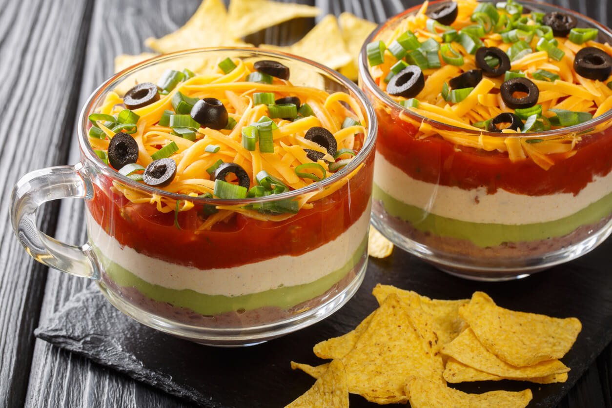 Classic Mexican 7 Layer Dip with corn chips close up in the glass.