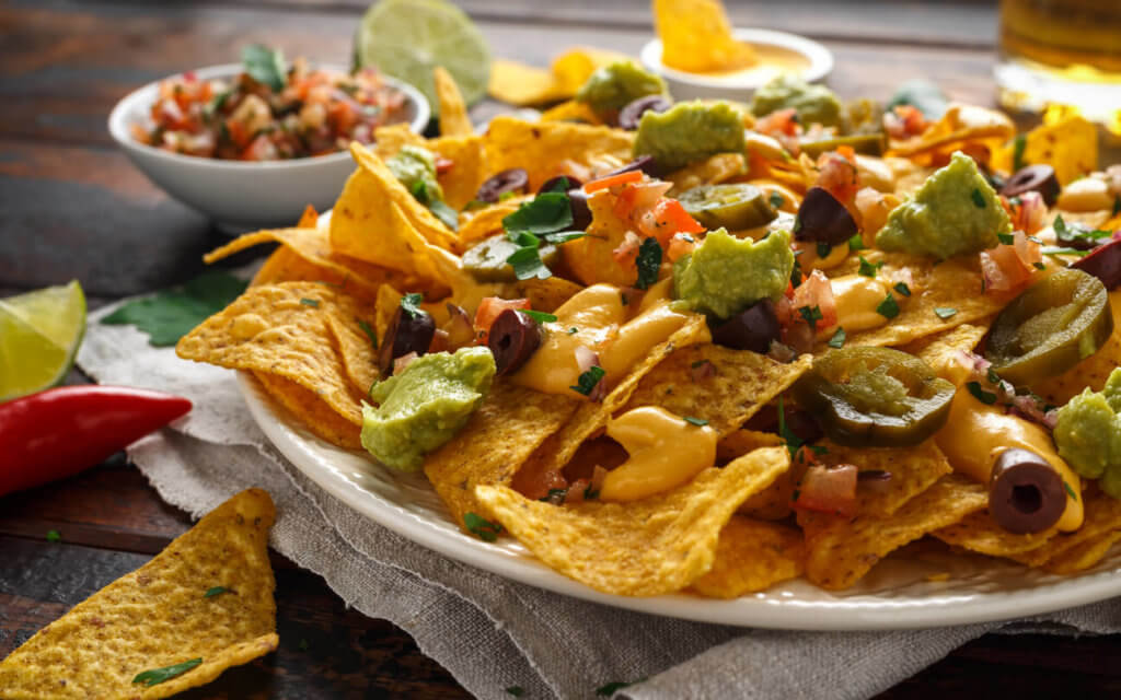 Mexican nachos tortilla chips with olives, jalapeno, guacamole, tomatoes salsa, and cheese dip.