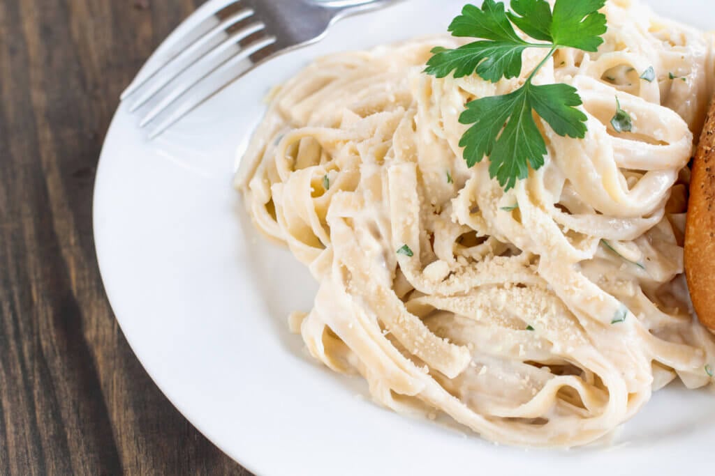 Plate of fettuccine Alfredo with fresh parsley and a slice of french bread. 