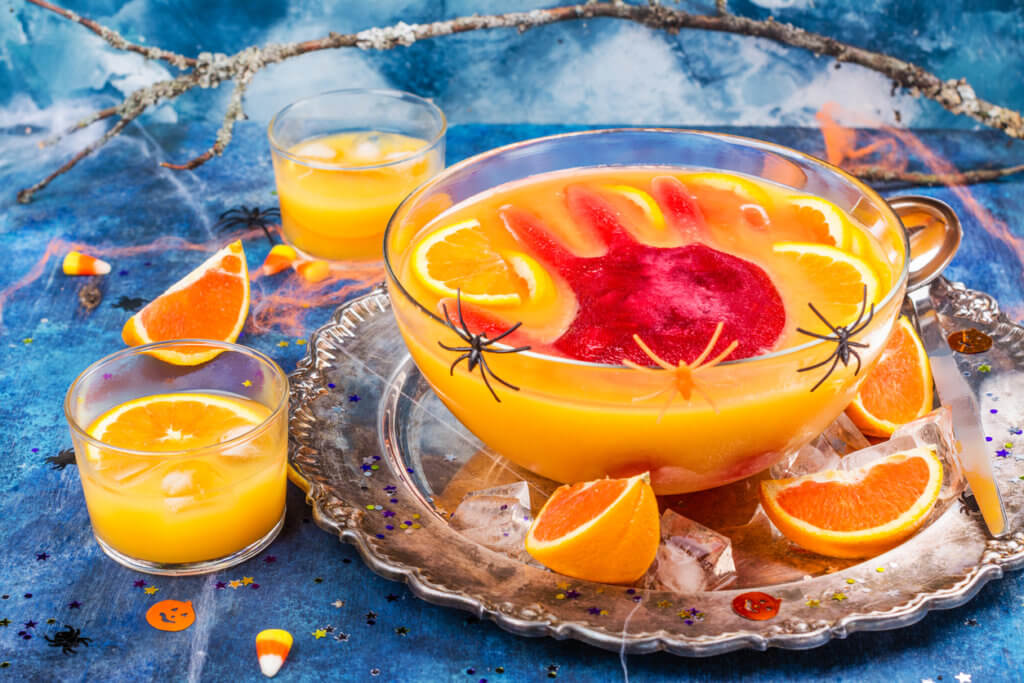 Ghoul's orange punch with bloody ice hand in a glass bowl on dark halloween background.
