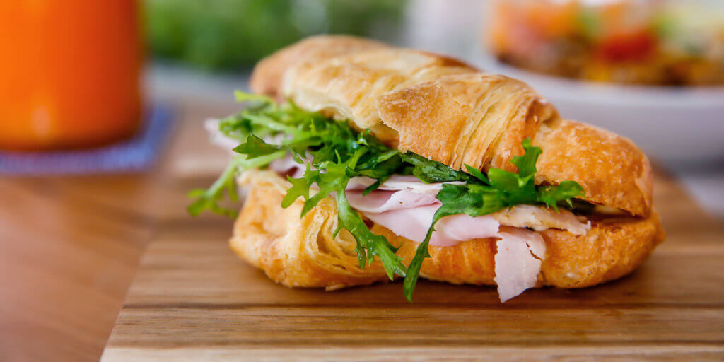 Close up croissant sandwich with ham and arugula for breakfast
