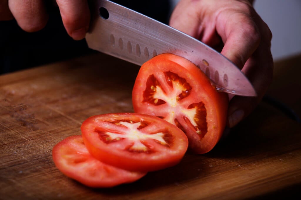 Tomato being sliced with a sharp kitchen knife.