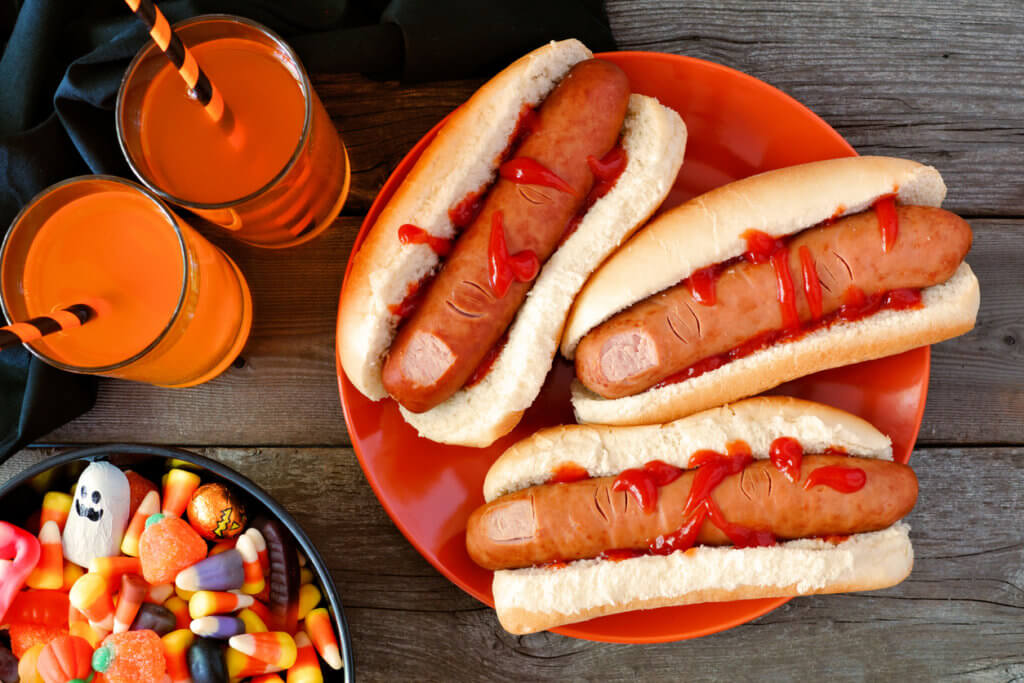 Halloween meal scene with hot dog fingers, drinks and candy.