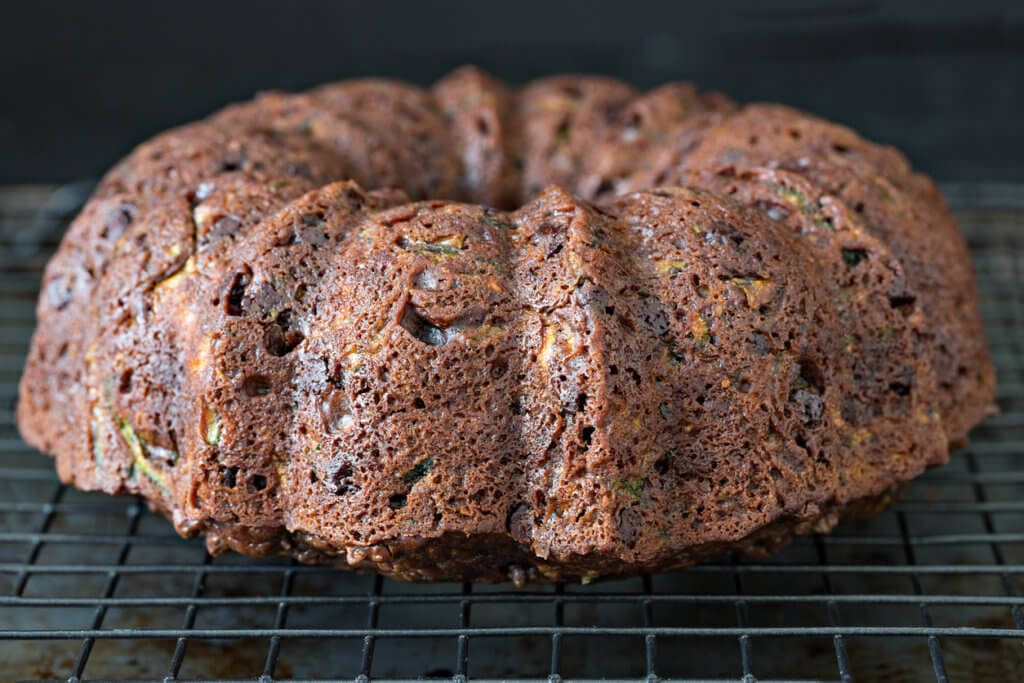 An extreme close up shot of a freshly baked chocolate zucchini bunt cake on a cooling rack.