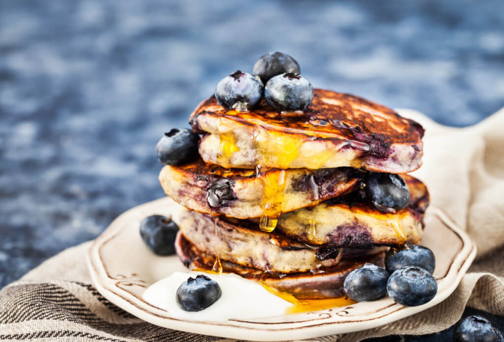 Stack of freshly prepared blueberry ricotta pancakes with fresh berries, yogurt and honey for breakfast