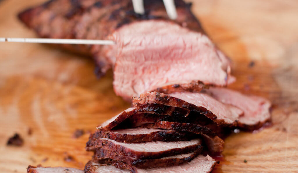 A Santa Maria style tri-tip being cut into slices with a knife and serving fork.