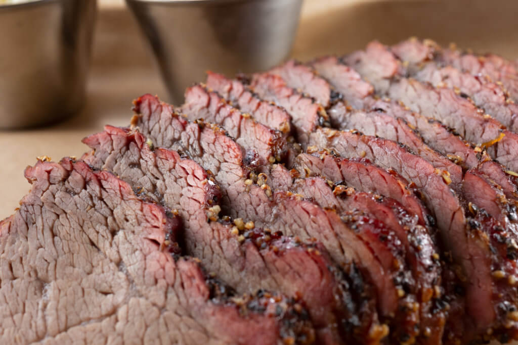 A closeup view of a tray of barbecue tri tip meat slices, in a restaurant or kitchen setting.
