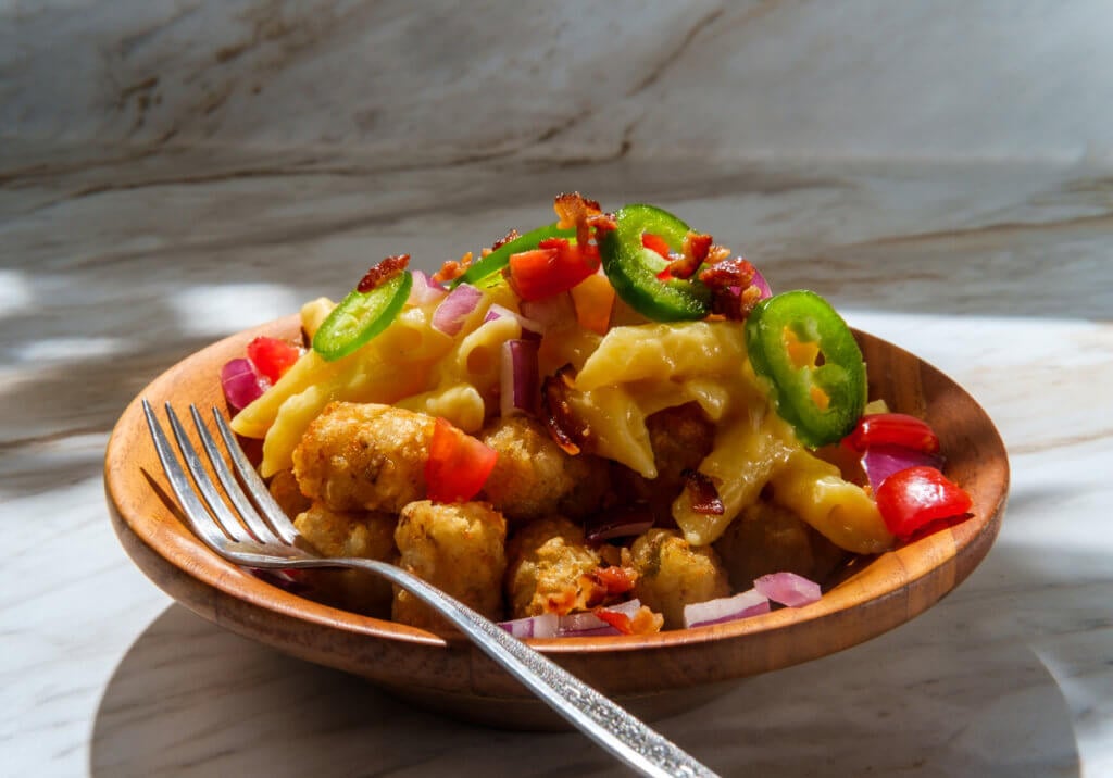 Fancy gourmet tater tot recipe topped with diced red onion tomato and jalapenos with crumbled bacon bits