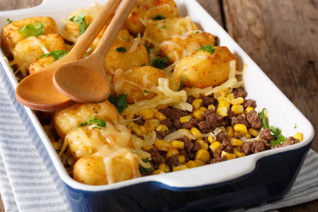 Homemade casserole of Tater Tots with minced beef, corn and cheese close-up in a baking dish.