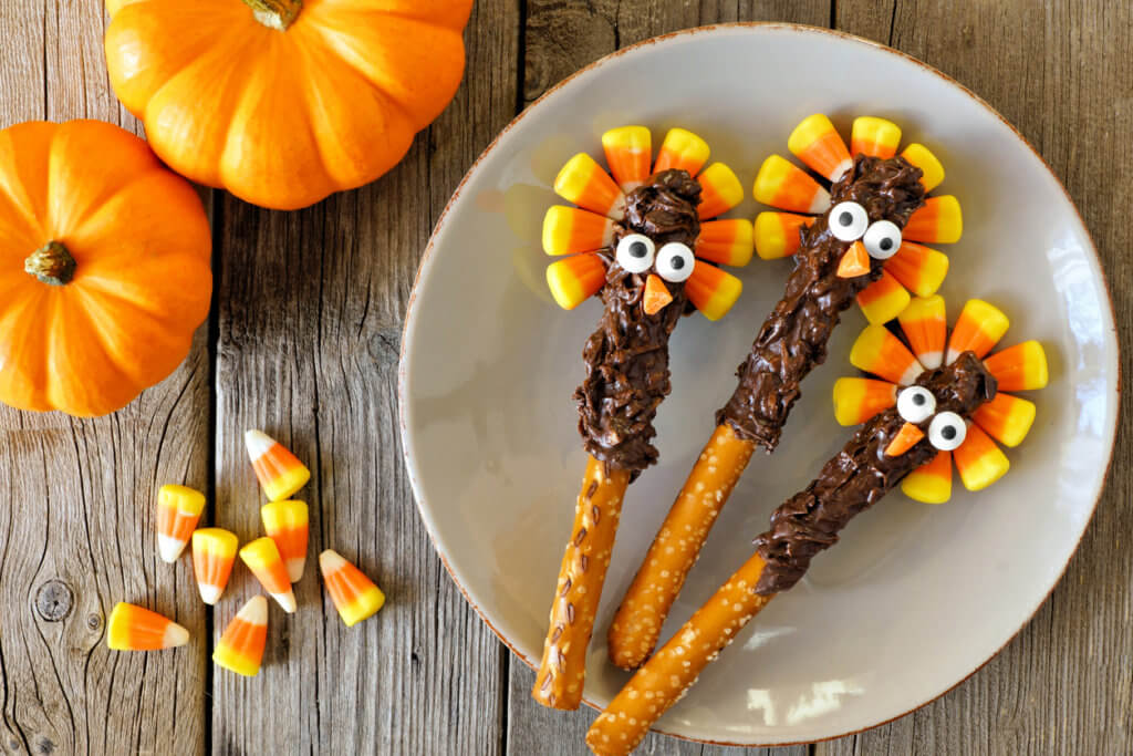 Cute Thanksgiving turkey pretzel sticks with candy corn, overhead scene on old wood.