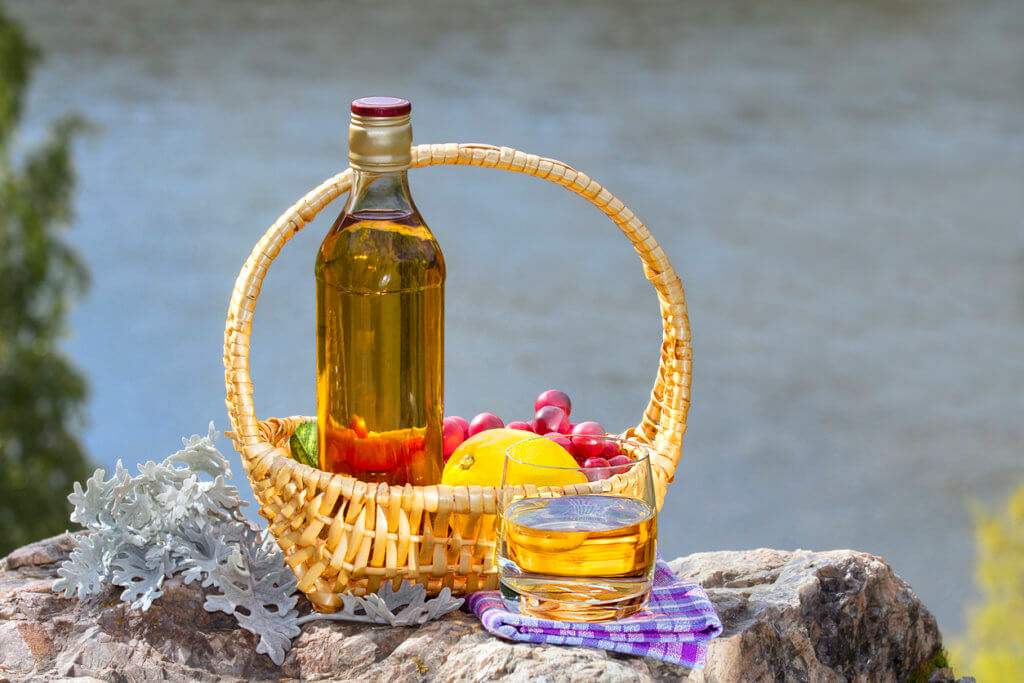 Bottle with the glass of whiskey and the basket with fruits on the rock by a river