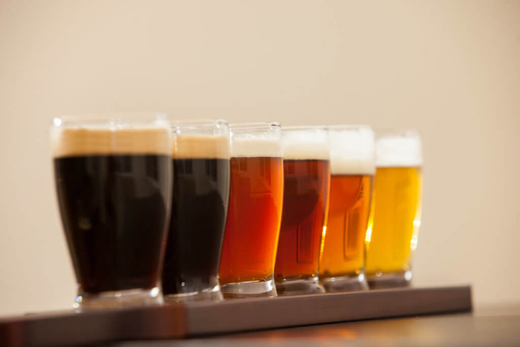 Six beer samples in small glasses on a bar.