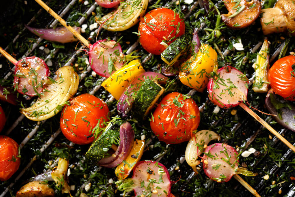 Grilled veggie skewers with cherry tomatoes, radishes, peppers and onions with fresh dill on a grill pan.