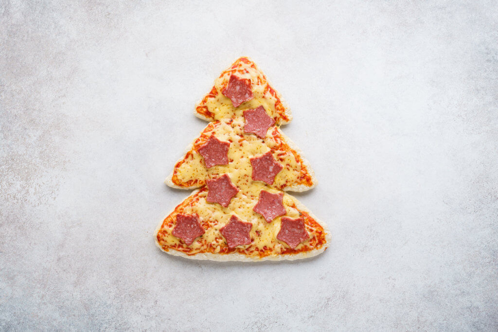 Pizza shaped as Christmas tree decorated with stars made of pepperoni. 