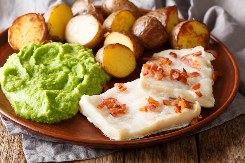 Cod Lutefisk with pea puree, baked potatoes and bacon close-up on a plate.