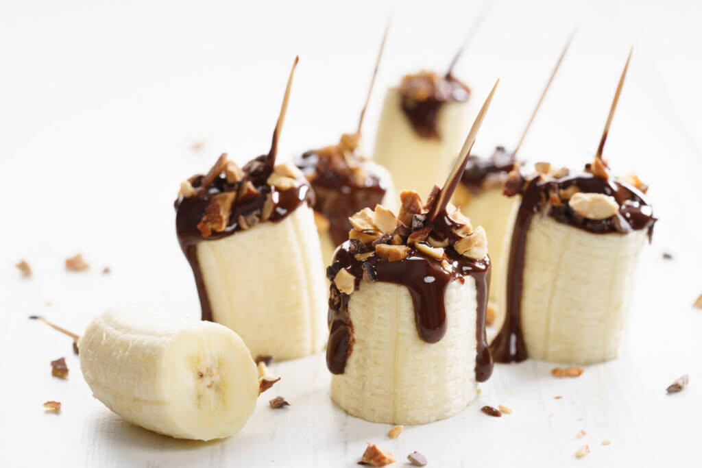 chocolate banana bites with chopped toasted almond topping on white wooden background.