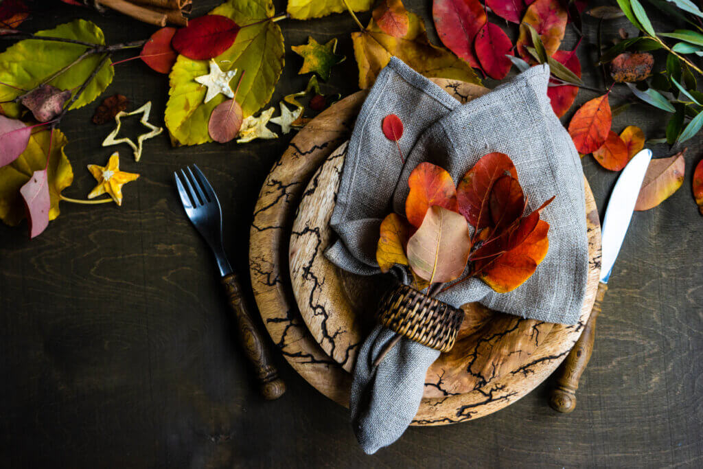 Autumnal place setting with yellow and red leaves on rustic background.