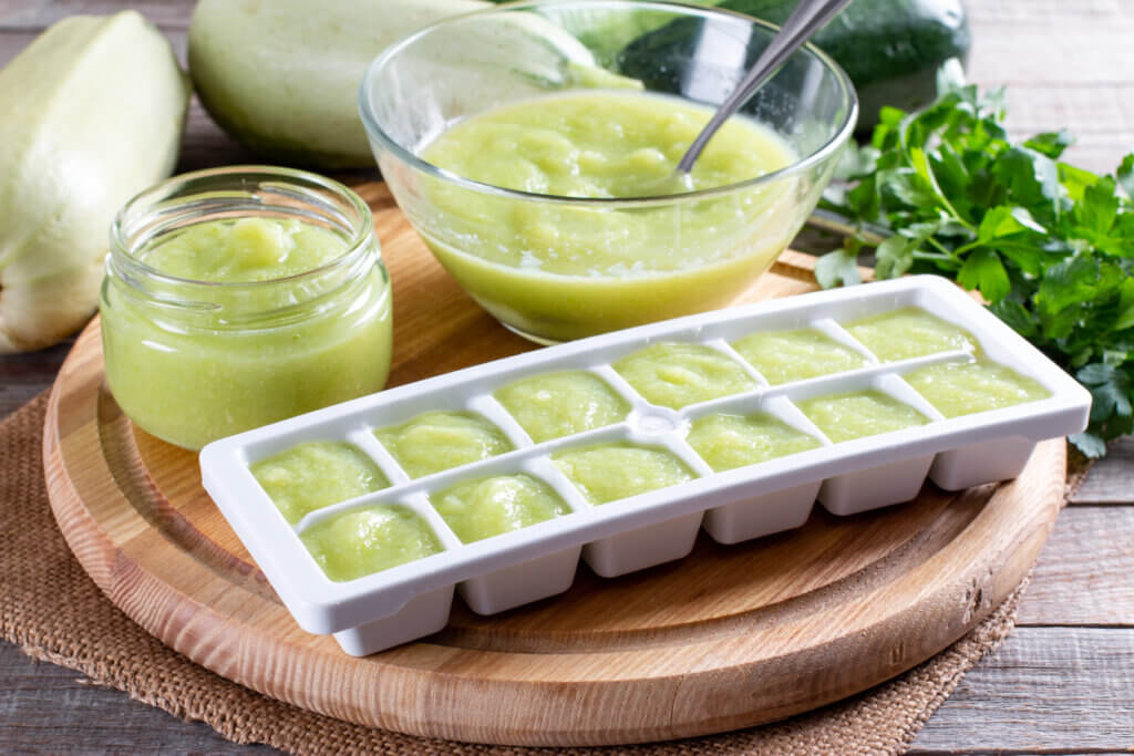 Zucchini puree in ice cube trays ready for freezing on a cutting board on a table.