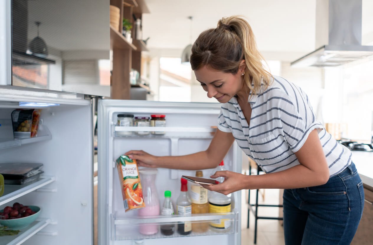 Woman at home adding things to her shopping list while checking the fridge