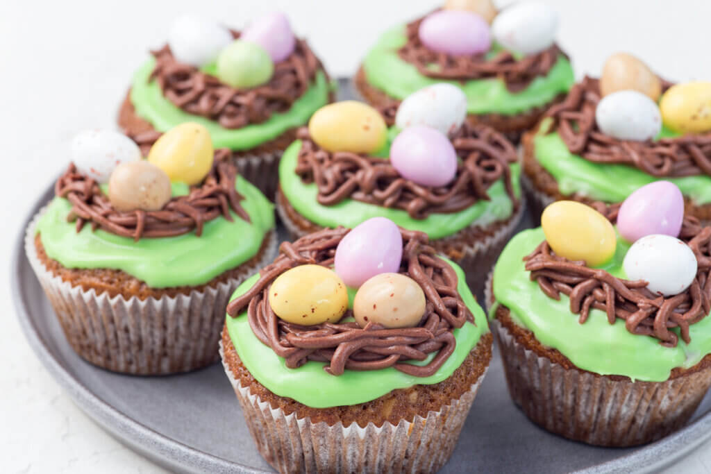 Carrot cupcakes with cream cheese frosting and Easter chocolate eggs, on gray plate, horizontal