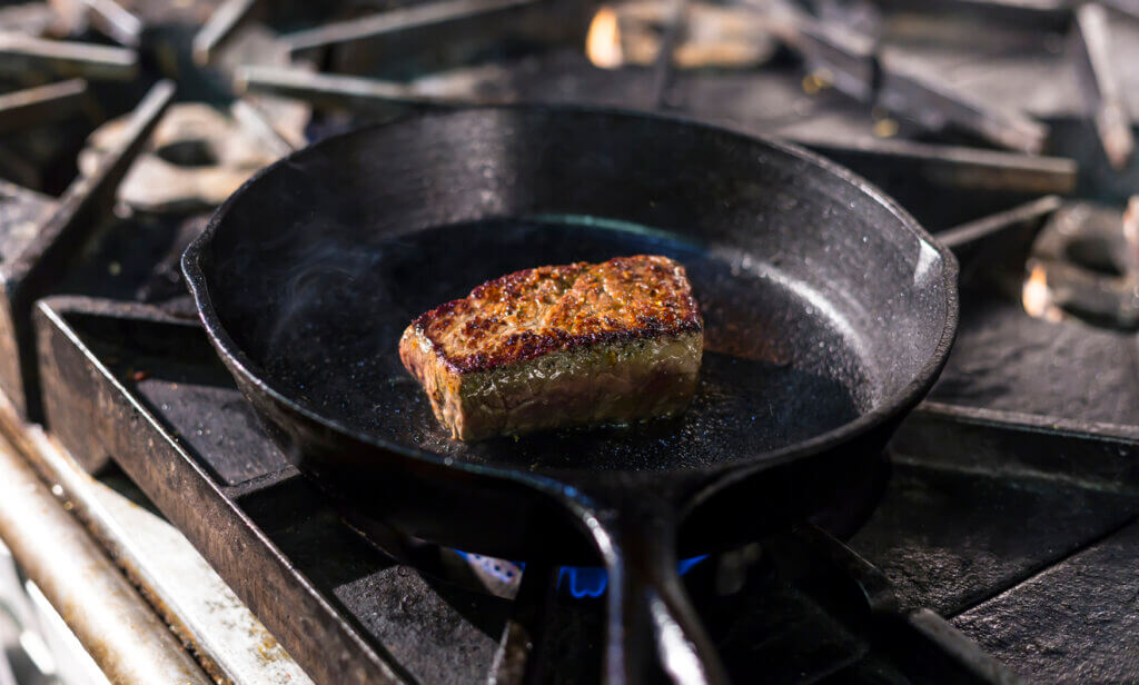 A steak sizzling in a casket iron skillet