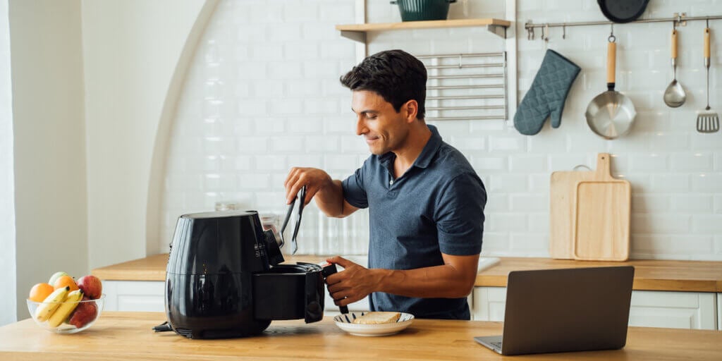 Man using air fryer and laptop in kitchen