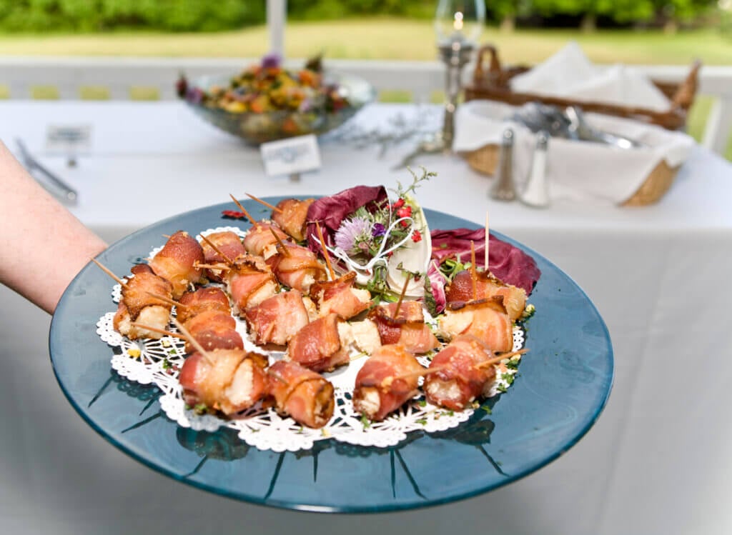 A waiter passes a tray of bacon wrapped scallop appetizers.