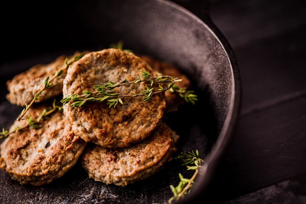 Sausage patties, seasoned with thyme leaves, in a cast iron skillet