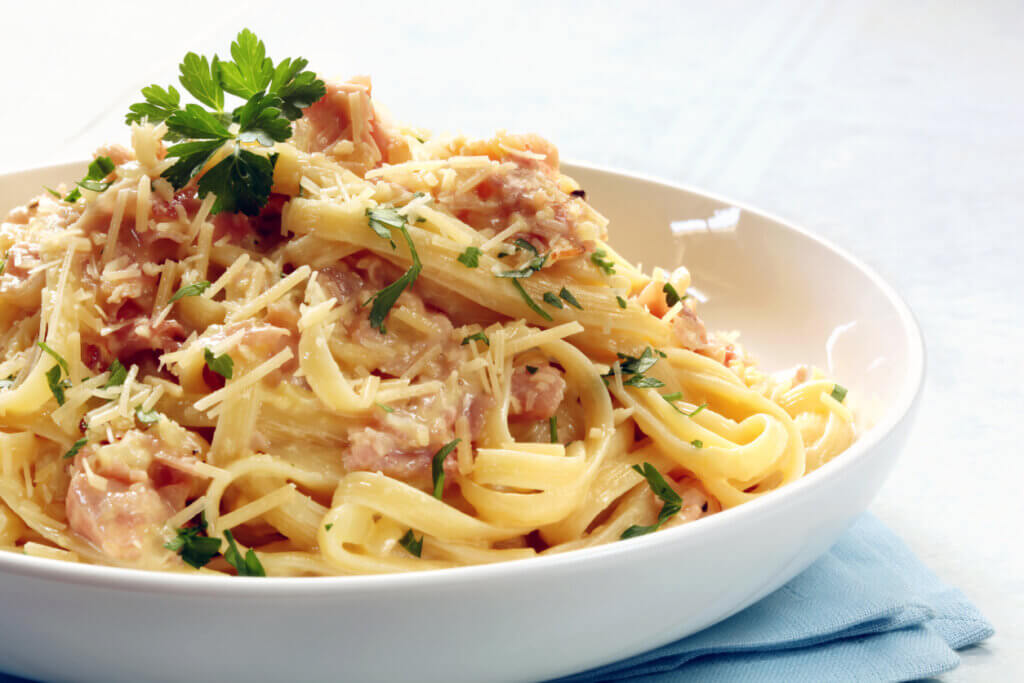 Fettucine carbonara in a white bowl, garnished with parmesan and parsley.
