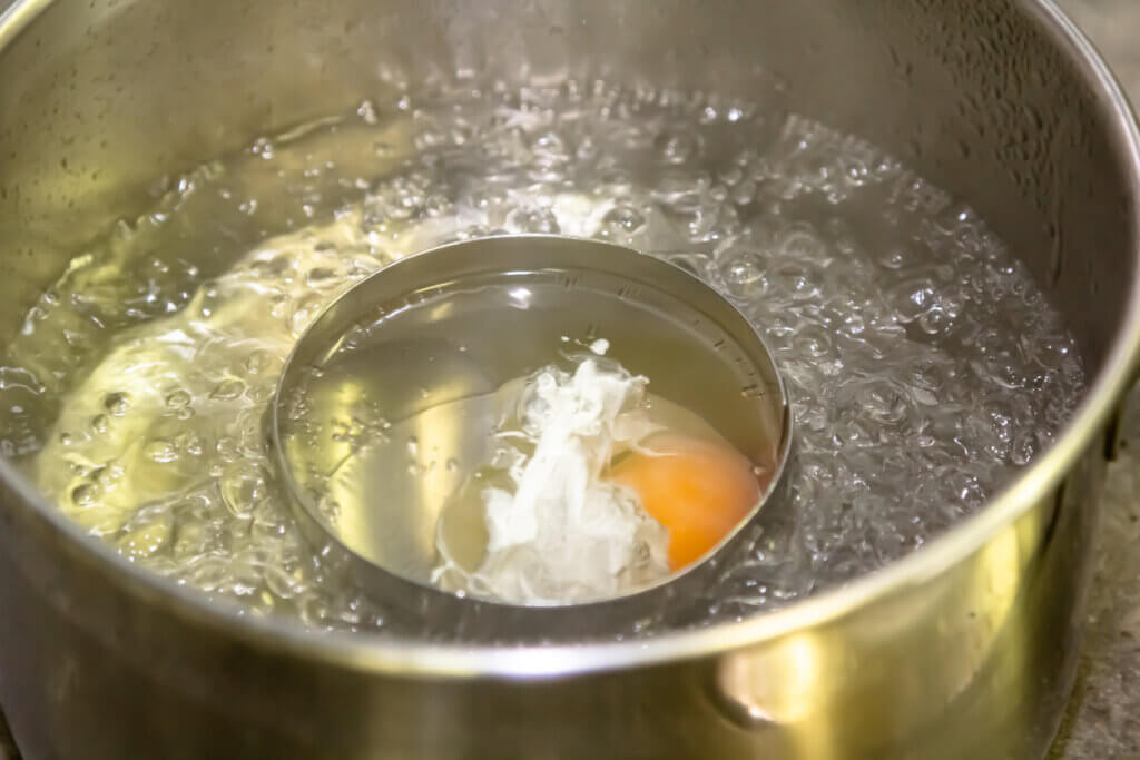 Poaching fresh eggs in a pan of water in an authentic kitchen environment.