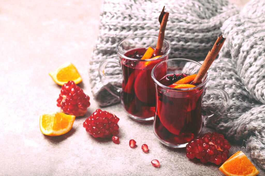 Hot mulled wine with apples, pomegranate, orange, anise and cinnamon with fresh fruits on slate marble background.