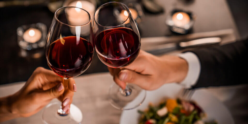 Close up of young couple toasting with glasses of red wine over dinner.