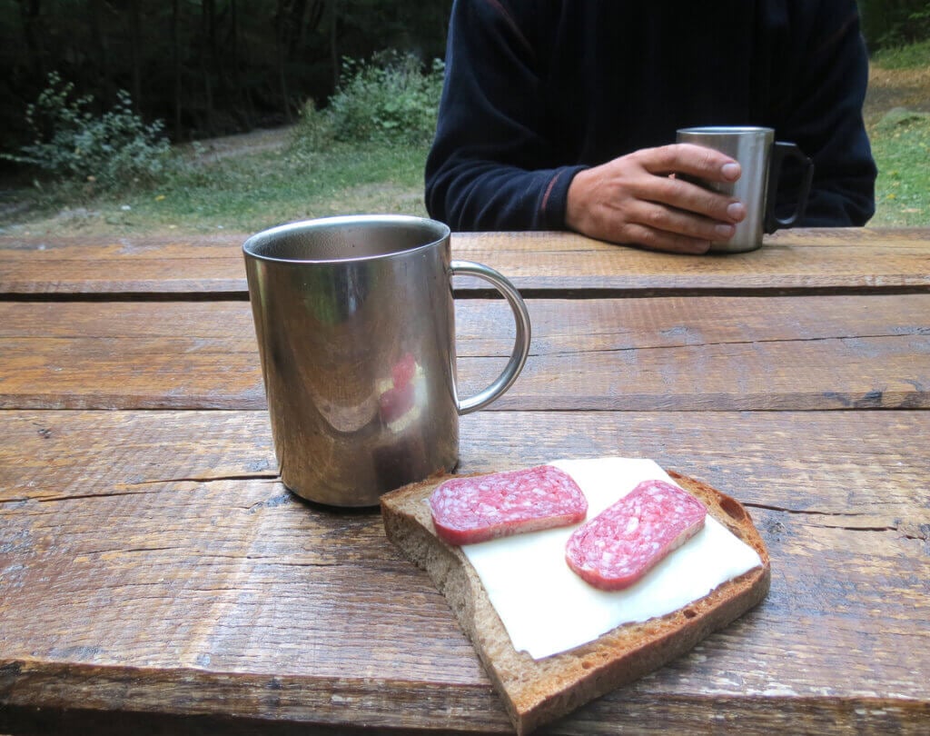 Man having his morninig meal, breakfast or lunch. Coffee in steel thermo mug and sandwich on wooden table.