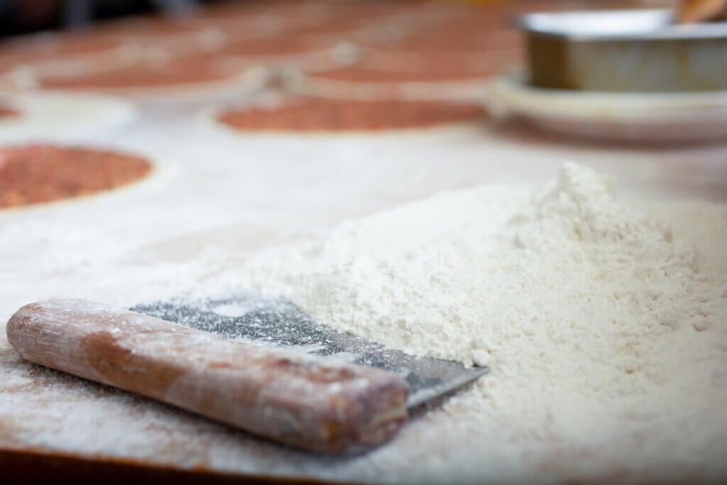 A closeup view of a big pile of flour on a rustic wooden table, in a kitchen setting.