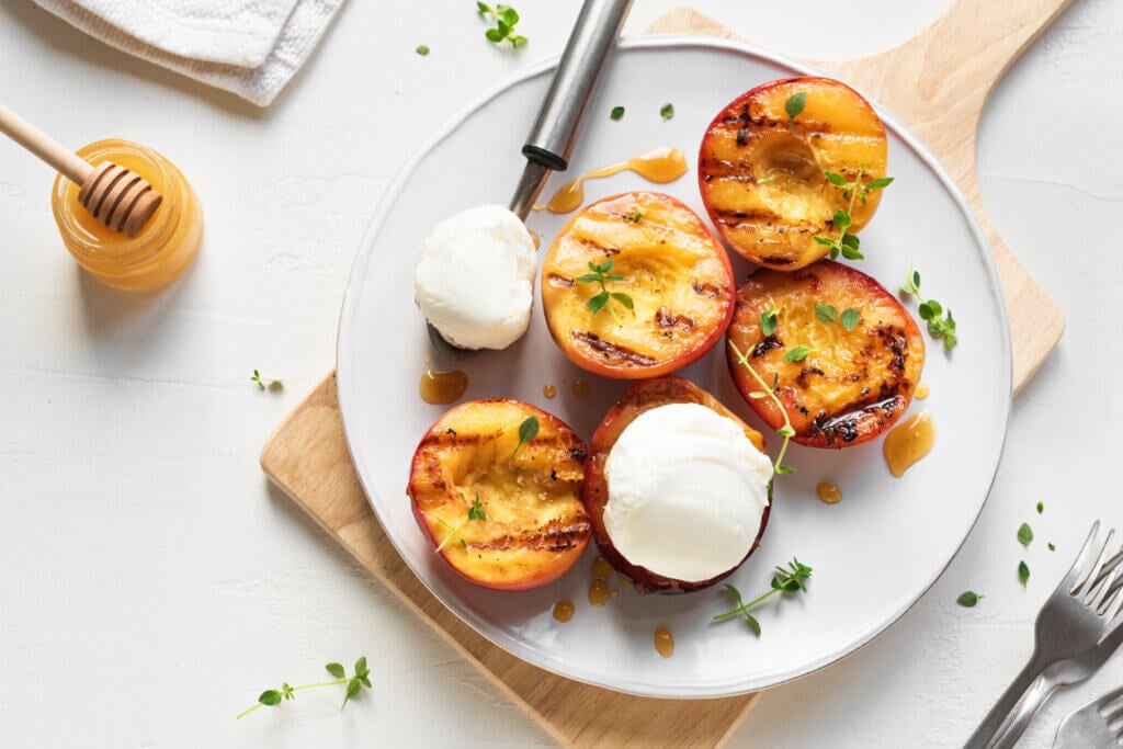 Grilled Peaches with Thyme, Honey and scoop of Vanilla Ice Cream on white plate.