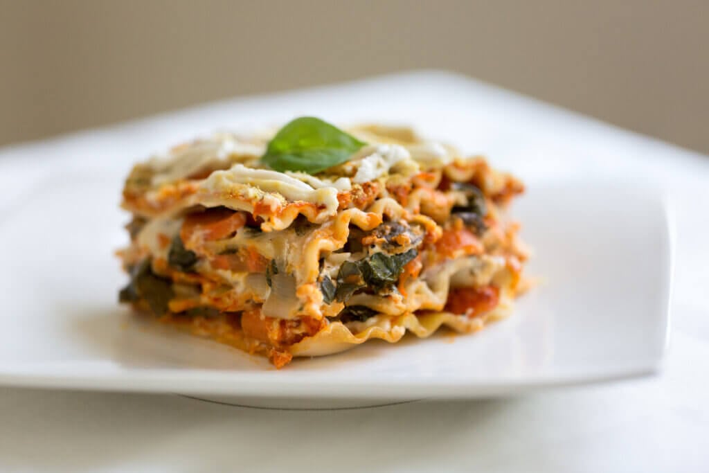 Vegan lasagna with vegetables, tomato sauce, cashew sauce and garnished with fresh basil and nutritional yeast.
