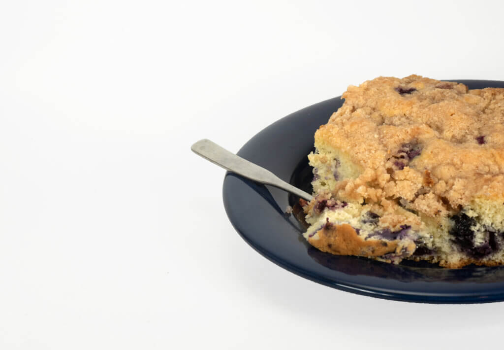 Classic blueberry buckle made with a silver fork on a dark blue plate against a white background