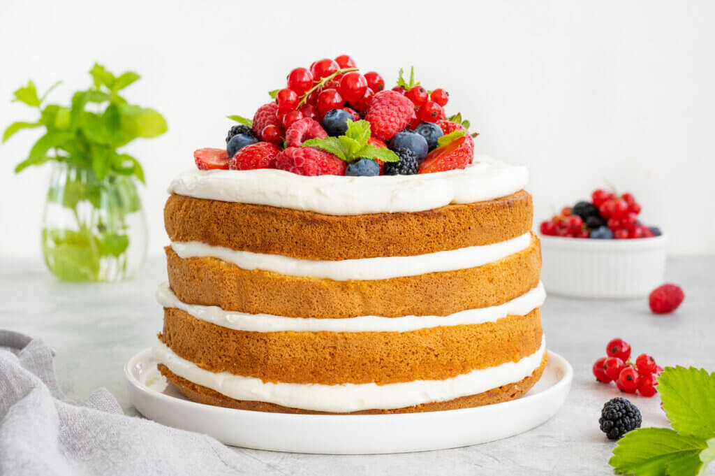 Homemade naked layered vanilla cake with whipped cream and fresh berries on top.