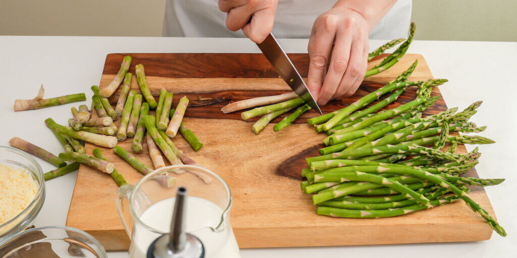 Woman hands cutting fresh green asparagus on wooden cutting board.