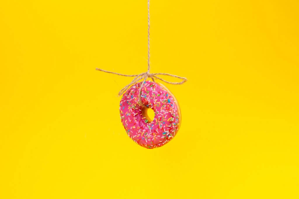 A round doughnut with pink frosting, suspended on a string.