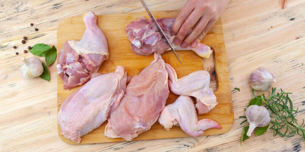 raw chicken being cut up on a wooden cutting board