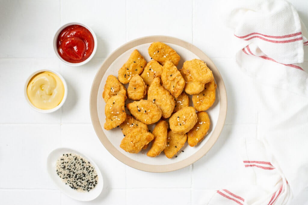 Chicken nuggets in a plate, ketchup and cheese sauce on a light background.
