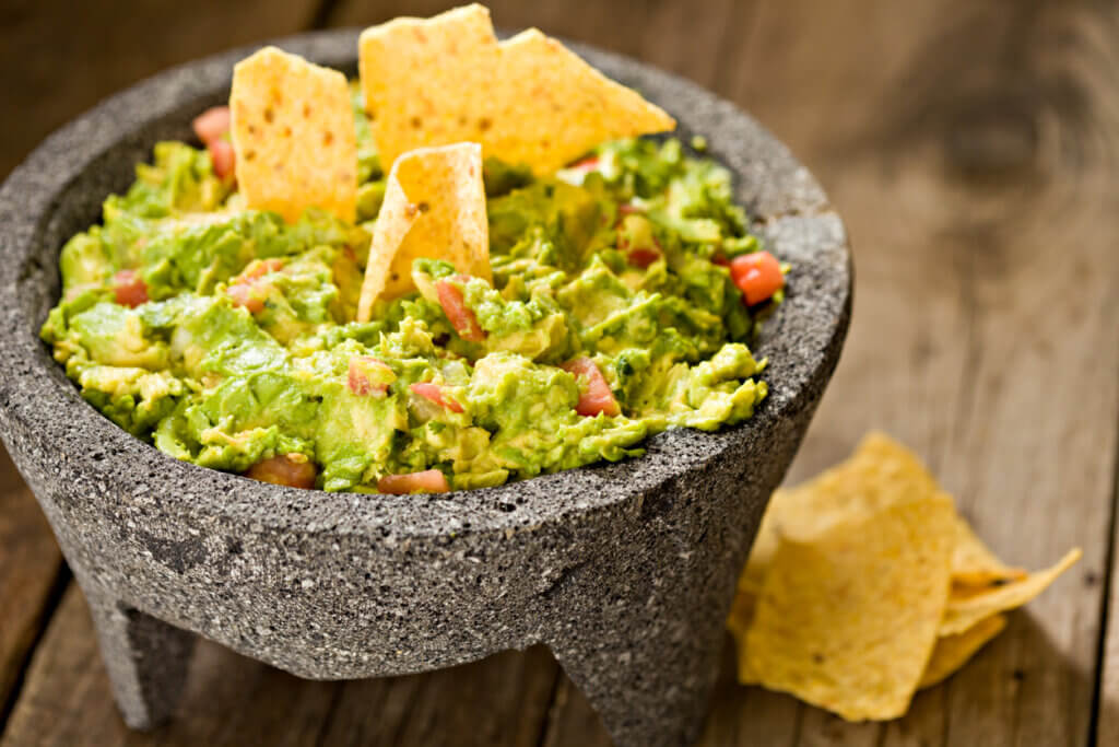 A high angle close up of creamy guacamole in a Mexican molcajete and crunchy corn chips.
