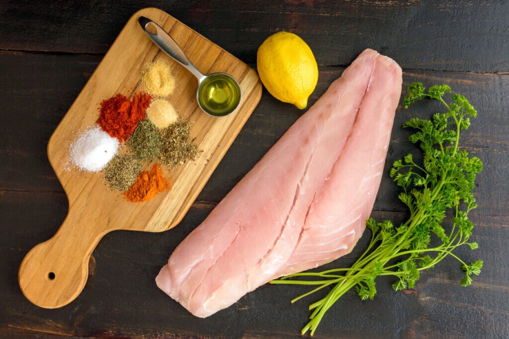 Raw snapper fillet, dried spices, and other ingredients to make a Cajun fish recipe.